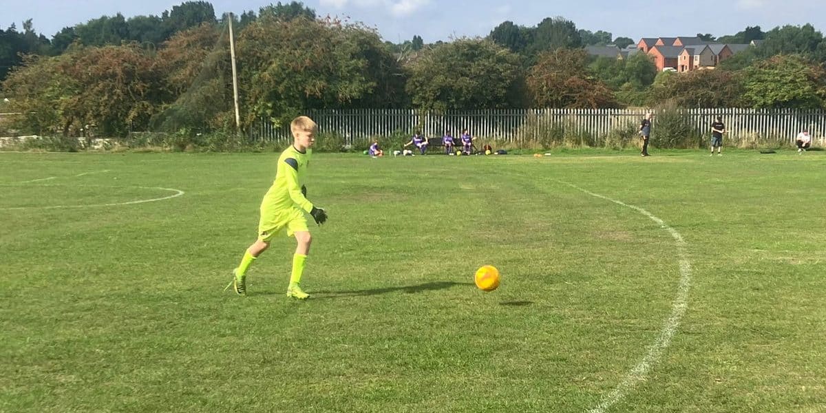 Young goalkeeper in bright kit on a football pitch during match.